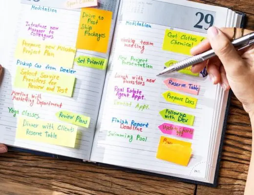 Open journal with notes and plans, a pen is in hand over journal