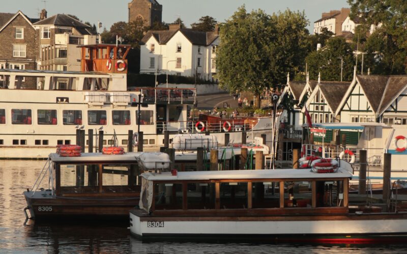Peaceful sunset scene at Lake Windermere with boats docked and golden light on the town.